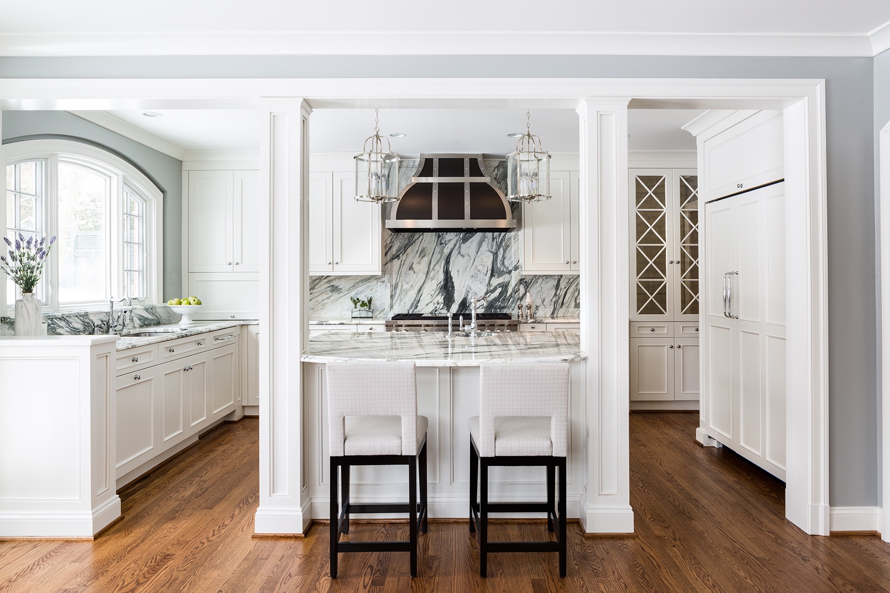 Kitchen island with white barstools, high-contrast white marble counters and backsplash, custom-built columns