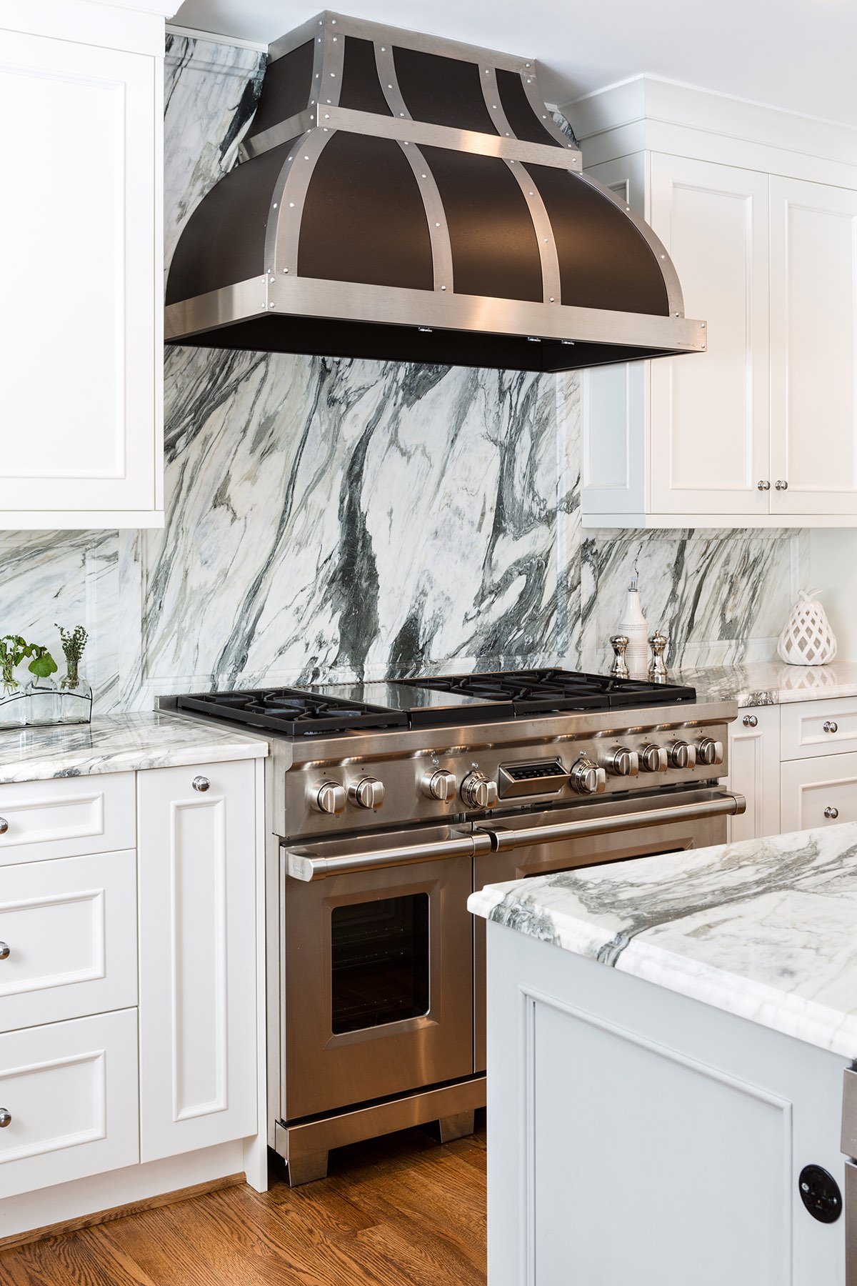 Home kitchen with stainless trim range hood, black-vein marble backsplash